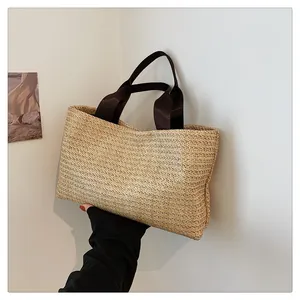 Detailed view of hand-woven straw tote bag with brown straps against a minimalist wall