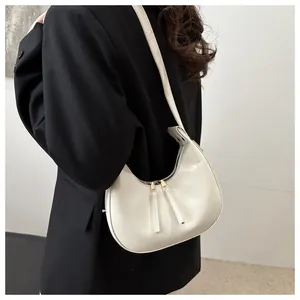 Side view of a minimalist cream-colored crescent shoulder bag worn with a black blazer