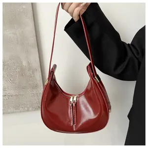 Detail of red crescent bag showing glossy patent leather and gold zipper accents