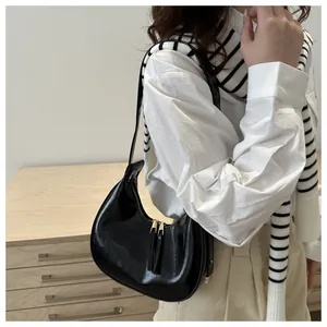 Detail of a black patent leather hobo bag with gold zippers worn on the shoulder