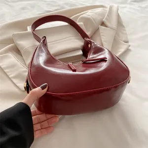 Deep burgundy glossy leather crescent shoulder bag with gold hardware and zipper