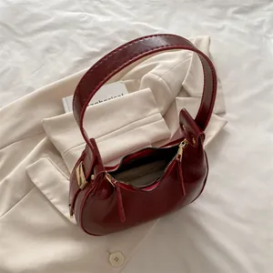 Fashionable dark red crescent shoulder bag in glossy patent leather on a beige blazer