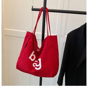 Détail d'un sac cabas en toile rouge avec lettrage blanc suspendu sur un cintre noir