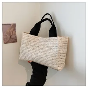 Detailed view of beige straw tote bag with black canvas handle against clean wall