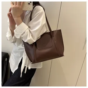 Detailed view of dark brown leather tote bag with round buckle on a white shirt model