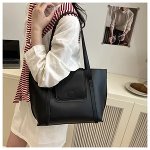 Detail of a black leather tote bag featuring a round decorative buckle in an office setting