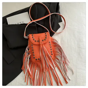 Détail du petit sac bohème à franges orange avec des rivets sur un fond texturé moderne