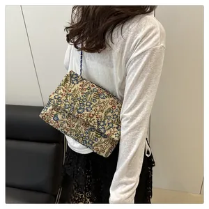 Floral jacquard shoulder bag with blue chain strap worn by a model in a minimalist setting