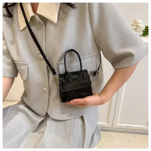 Detail of a mini black crossbody bag featuring glossy crocodile texture and small handles
