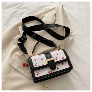 Detail of white leather cherry print crossbody bag with contrast trim and cherry charm