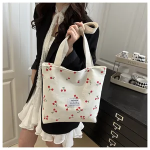 Close-up of beige corduroy tote bag featuring red cherry prints and white woven label