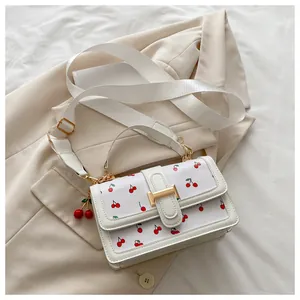Close-up of cherry print crossbody bag with gold buckle on a beige blazer background