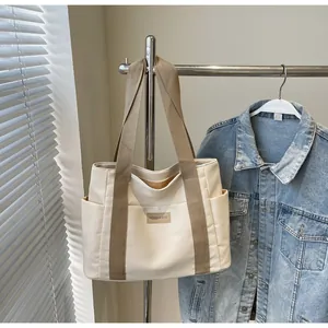 Vista dettagliata della borsa tote in tela bianco sporco con tasche laterali e logo in pelle