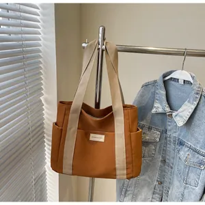 Dettaglio della borsa tote in tela caramello con manici beige e tasche laterali