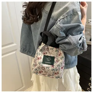 Détail d'un sac seau en toile à fleurs avec écusson vert et bandoulière noire robuste