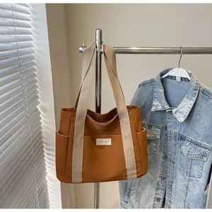 Dettaglio borsa tote in tela kaki con manici color crema ed etichetta logo frontale