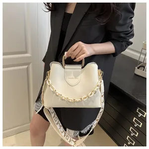 Detail of off-white crossbody bag with gold U-handle and wide patterned fabric strap