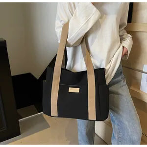 Vista laterale di una borsa tote in tela nera con tasche laterali ed etichetta in pelle