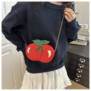 Detalle del bolso bandolera de cereza roja con hojas verdes y cadena de metal dorado