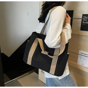 Borsa tote nera in tela con manici kaki e tasche laterali indossata a spalla