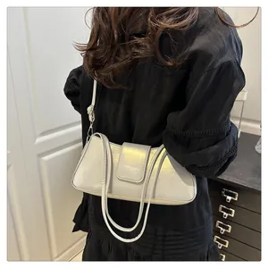 Detail view of a silver patent leather underarm bag worn on a shoulder against a black dress