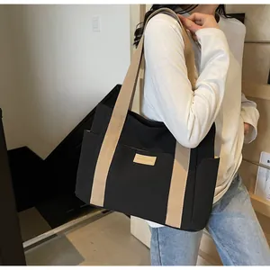 Dettaglio della borsa tote in tela nera con tasca laterale e tracolla color crema