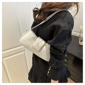 Model wearing a minimalist cream patent leather underarm shoulder bag with embossed detail