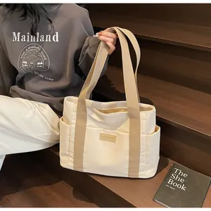 Dettaglio della borsa tote in tela crema con tasche laterali e logo in pelle decorativo