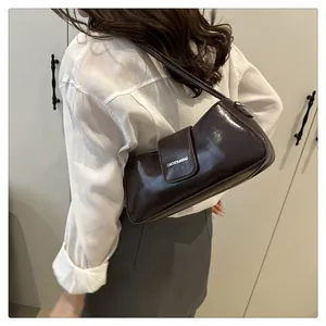 Detail of dark brown glossy patent leather baguette bag worn over the shoulder