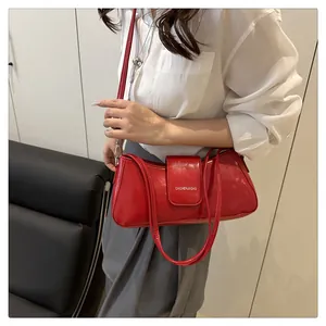Close-up of a glossy red patent leather shoulder bag with silver logo worn by a model