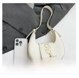 Borsa a mezzaluna bianca con fibbia dorata e frange accanto a uno smartphone per scala