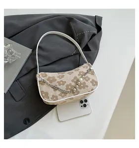 Detail of beige shoulder bag featuring floral patterns and a pearl silver chain strap