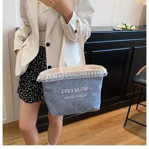 Détail d'un sac cabas en denim bleu clair avec bordure en dentelle blanche et lettrage