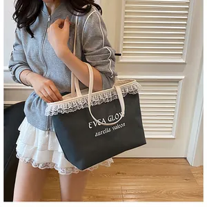 Détail d'un sac cabas noir avec bordure en dentelle blanche et lettrage sur bandoulière