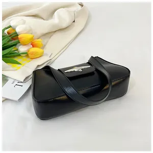 Vue à plat d'un sac d'épaule en cuir noir avec boucle oiseau à côté de tulipes fraîches