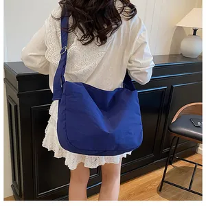Detailed back view of a dark blue large canvas crossbody bag worn by a model in a room