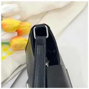 Gros plan sur la boucle en métal argenté et le cuir noir grainé du sac à bandoulière