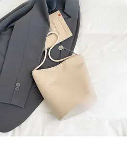 Gros plan détaillé du sac seau en cuir beige avec bandoulière corde et chaîne métallique