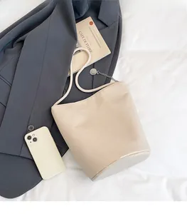 Comparaison de taille détaillée entre le sac seau beige et un smartphone sur fond blanc
