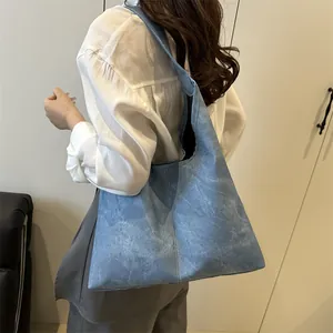 Minimalist light blue denim tote bag with washed texture shown on shoulder