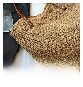 Detail of hand-woven straw beach bag with brown faux leather handles and X-stitch sewing