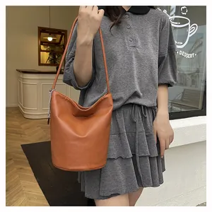 Detail of caramel leather bucket bag with pebbled texture and silver chain charm