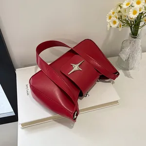 Détail du sac bandoulière en cuir rouge avec boucle étoile argentée sur un livre déco