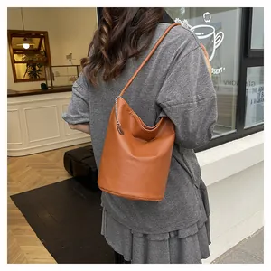 Detail view of brown pebbled leather bucket bag with silver chain and round charm decoration