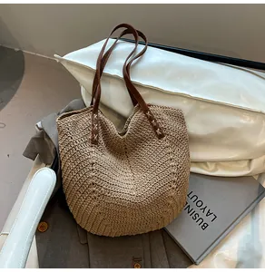 Detail of woven straw tote bag featuring brown leather handles and geometric texture