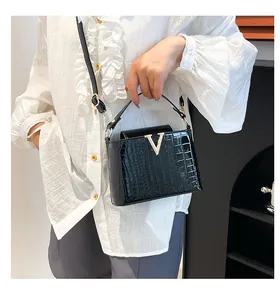 Detail of glossy black crocodile pattern handbag with elegant gold V-shape metal buckle