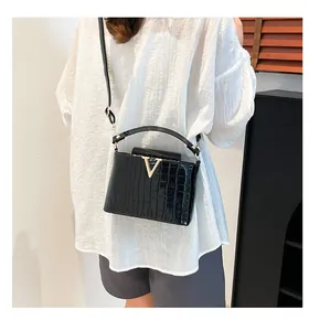 Detail of black crocodile embossed handbag with golden V-shaped buckle on polished leather