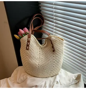 Detailed close-up of woven paper rope texture and brown leather straps on a beige tote bag