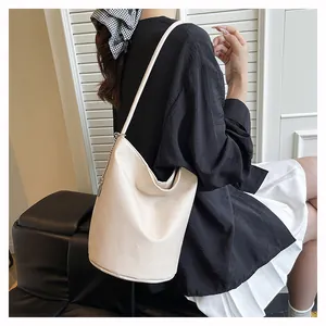Chic cream litchi grain bucket bag styled on shoulder with minimalist black outfit