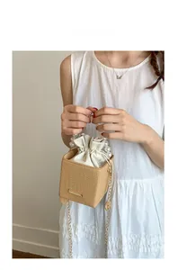 Close-up of woven bucket bag featuring pearl top handle and gold chain strap detail
